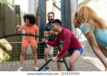 Battle rope training in training, Asian man using rope while multiracial friends encourage him to go on.