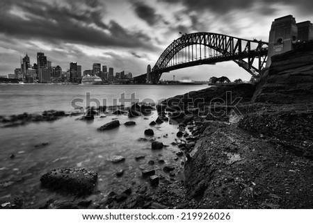 australia sydney city landmarks harbor bridge and CBD at sunset with blurred clouds low tide wet sea bottom rocks Royalty-Free Stock Photo #219926026