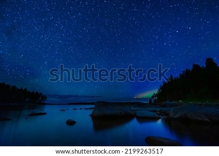 night landscape with a starry sky and Milky way with many bright stars. Astrophotography with constellations and galaxies over water of a lake with rocks and a forest on background