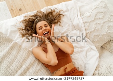Playful girl having fun and making grimaces while chilling in her bed. Top view. Cozy home. Lying on back. 