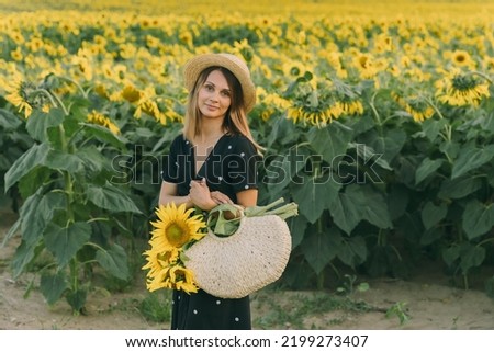 Girl in a field of sunflowers in the sun. Girl collected a bouquet of sunflowers. Girl is wearing black polka dot dresses. She hold 
wicker bag. In the background is blurred field of sunflowers. 