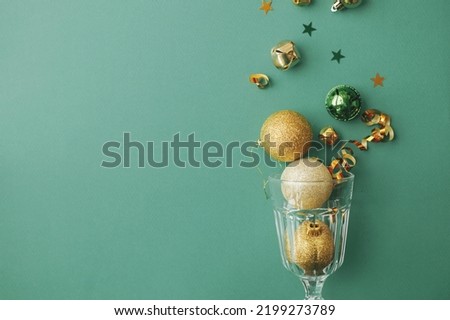 Happy New year and Merry Christmas! Stylish christmas gold baubles and confetti pouring from champagne glass on green background flat lay. Creative season's greeting card, space for text