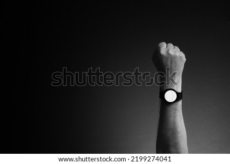 Black and white image of man's hand with smart watch on wrist, displaying blank white screen, isolated on dark background with copy space