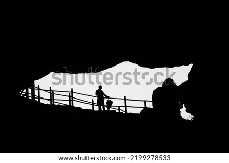 silhouette of a standing man with umbrella on a railing. The picture was taken from a cave in the direction of the exit. Black and white picture