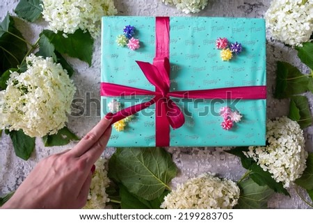 woman hand, hydrangea flower, green turquoise color gift box with red ribbon bow on grey wooden background. Concept: holiday, celebration, birthday, New Year, Christmas, Valentines Day, Mothers Day, 