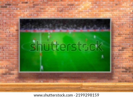TV with soccer field on brick wall and wooden table with empty space. Selective focus. Blurred background.