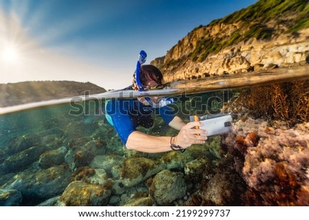 Snorkeller taking pictures underwater with a cellular phone in a waterproof bag Royalty-Free Stock Photo #2199299737