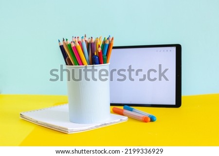 Tablet and notebook for online study on yellow and blue, home education art class, supplies on desk and container, copy space 