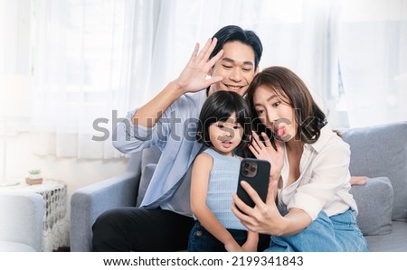 Portrait of happy asian family with toddler girl child use smartphone selfie say hi virtual in living room. Happy live online influencer blogger. Technology connected people family lifestyle concept Royalty-Free Stock Photo #2199341843