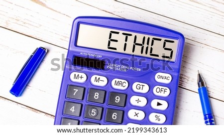 Flat lay or top view of blue pen and calculator with ETHICS text on light wooden table.