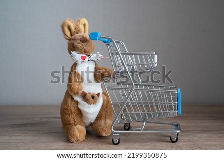 miniature kangaroo plush toy with shopping cart on a gray background, concept of shopping for kids, children, online commerce, e shopping