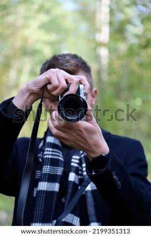 Photographer in a black coat and scarf with a camera at work. Guy takes pictures on the camera. The photographer guy in a coat and scarf shoots at the camera.