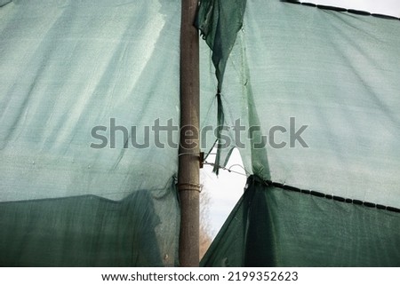 Torn grid in stadium. Green grid around site. Torn fabric. Hole in grid.