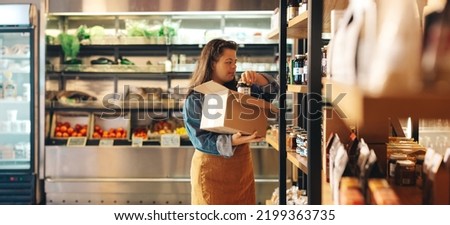 Shop employee with Down syndrome restocking food products in a grocery store. Empowered woman with an intellectual disability working as a shopkeeper in a local supermarket.