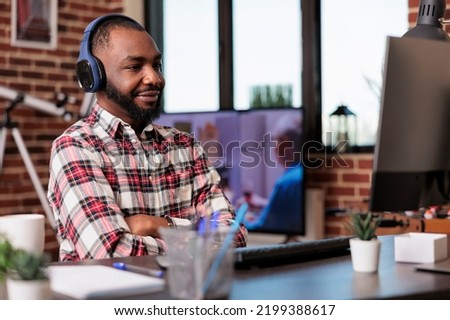 Male freelancer using headphones and working remotely on computer at home desk. Listening to music or podcast show online on social media internet, attending class lesson webinar.