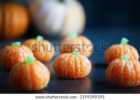 Halloween cute pumpkin orange fruit with gummy candy stem. Healthy dessert snack with funny faces for child's party decoration. Selective focus on center with blurred foreground and background.
