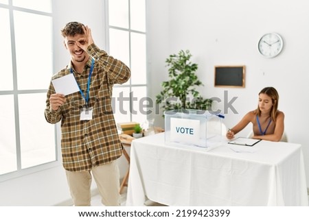Young handsome man voting putting envelop in ballot box smiling happy doing ok sign with hand on eye looking through fingers 