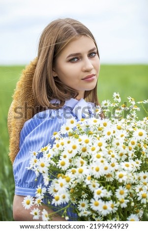 close up portrait of a young blonde girl with a bouquet of chamomile in a field