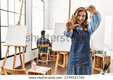 Young artist woman at art studio smiling making frame with hands and fingers with happy face. creativity and photography concept. 