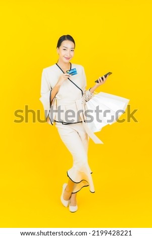 Portrait beautiful young business asian woman with shopping bag from department store and mall on yellow background