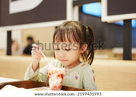 Little asian girl eating ice cream at restaurant. Soft focus. Copy space.