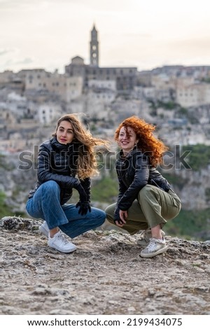 Young smiling women friend couple portrait with Matera city in the background at sunset. 