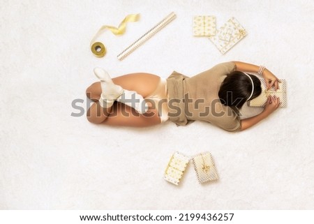 Beautiful young woman in gold sweater,  panties and socks wrapping christmas gifts boxes lying on fluffy snow-white carpet. Top view.