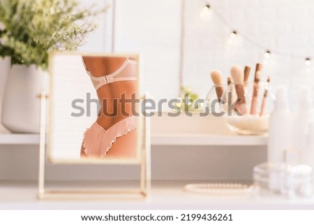 Reflection in table mirror of woman body in underwear. Female party preparation. Сhristmas, light bulbs, eucalyptus, fir,  pine branches in a vase  on dressing table with make up accessories. 