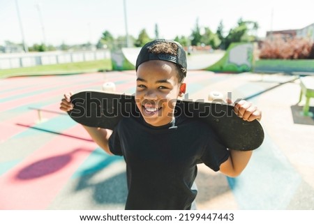 A black boy with black t-shirt posing with his skateboard with the sky in the background