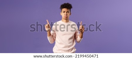 Portrait of gloomy, pouting frowning hipster guy dont have something he wants, pointing fingers up at super cool expensive thing, asking for it, trying receive compassion, purple background Royalty-Free Stock Photo #2199450471
