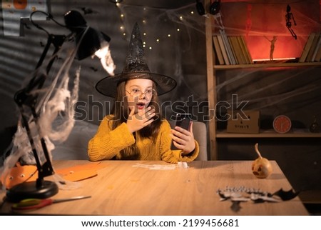 Portrait of scared girl in witch hat looking at mobile phone seeing bad news, photos or message. Worried teen grabbing head at darkness room on Halloween. Human reaction, expression