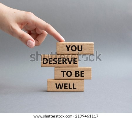 You deserve to be well symbol. Wooden blocks with words You deserve to be well. Beautiful grey background. Businessman hand. You deserve to be well concept. Copy space.