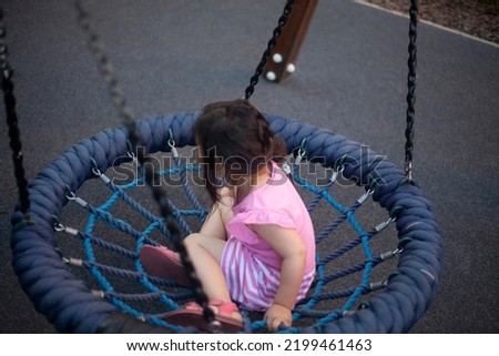 Child on round swing. Children's playground for children. Asian girl swings merrily. Preschooler plays in courtyard in summer. Safe swing for young children.