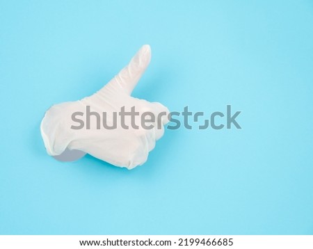 A female gloved hand sticks out through a blue paper background and shows a thumbs up.
