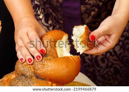 A woman's hand breaks a challah on a wooden board on the Shabbat or Rosh Hashanah holiday. Horizontal photo