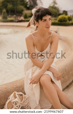 Nice young caucasian girl spending free time outdoors in city. In summer, brunette wears loose dress. Lifestyle concept