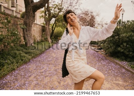 Positive young caucasian woman enjoys walking outdoors in summer. Brunette wears sundress, shirt and bag. People emotions, lifestyle and fashion concept
