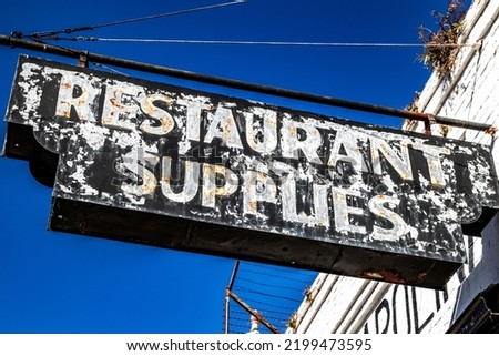 Old weathered vintage restaurant supplies sign hanging over a store entrance clear blue sky