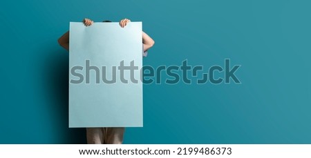 unrecognizable person holding a big blank poster standing against the wall, mockup template
