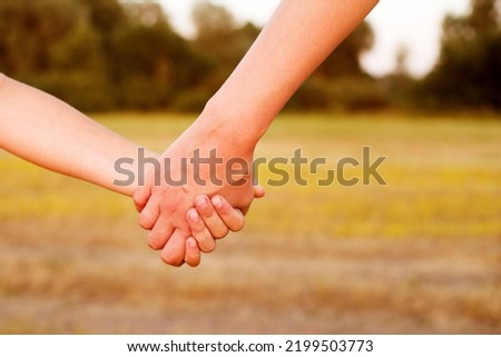 Children's hand holds mother's hand against the background of a yellow field on a summer sunny day, close-up, soft focus. Family scene, child care, support and guardianship Royalty-Free Stock Photo #2199503773