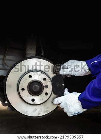 Mechanic holding brand new brake pad near assembled disc brakes. Vertical banner for Replacement of brake system consumables with copy space