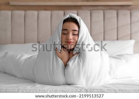 Beautiful young woman covered with warm blanket on bed at home Royalty-Free Stock Photo #2199513527