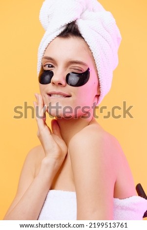 Horizontal photo, a woman with perfect skin on an orange background in a towel on her head and body with black patches on her face smiles playfully