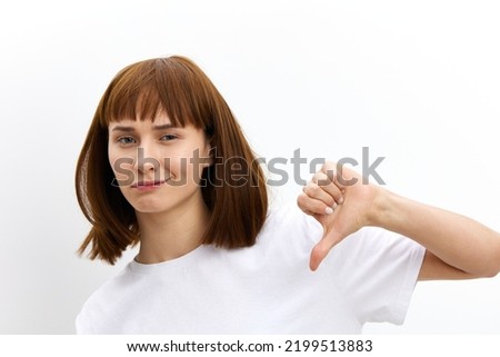 a funny, funny, cheerful woman stands on a white background in a white T-shirt and shows her thumbs down as a sign of disapproval. 