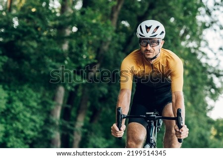 Sporty man wearing active wear and helmet riding a black bike in nature. Concept of people, workout and favorite hobby. Copy space. Looking into the camera. Royalty-Free Stock Photo #2199514345