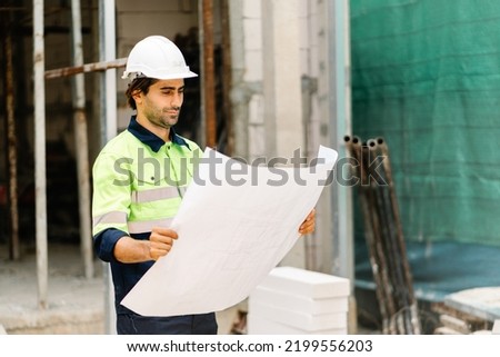 Construction worker in hardhat and vest with blueprint on construction site