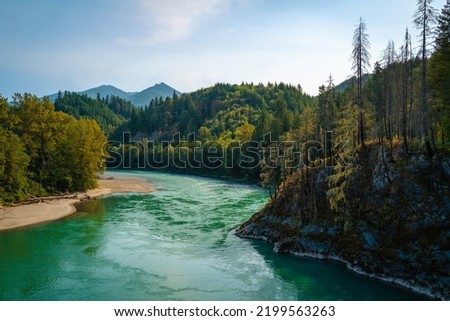 Panoramic landscape of turquoise-colored Skagit River water and green forest toward Glacier Peak over the Concrete Sauk Valley Bridge in Concrete, Washington State Royalty-Free Stock Photo #2199563263