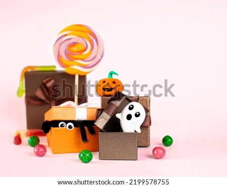 gift boxes with halloween symbols, lollipops and candies on a pink background close-up