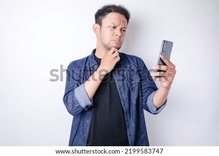 A portrait of an Asian man wearing a navy blue shirt looks so confused, isolated by a white background  Royalty-Free Stock Photo #2199583747