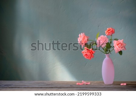 pink roses in glass pink vase on wooden table on background dark wall